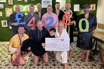 A photo of a group of Christie Charity fundraisers from Knutsford bar Dexter and Jones. 7 men are standing at the back in dressing robes holding numbers which read £4260. 3 men are kneeling at the front, also wearing dressing robes and holding a woman. The woman is holding a cheque reading "The Christie, Four Thousand Two Hundred and Sixty Pounds. Dexter and Jones Charity Calendar 2024".