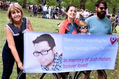 A photo of Christie fundraiser Michelle Foster holding a banner with a woman, a man and a small child. The small child is sitting on a bike, which is behind the banner. The banner reads, "Thank you for supporting the Young Oncology Unit at The Christie. In memory of Josh Hallam, forever loved."