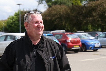 A photo of David Kenny, car park supervisor at The Christie, standing in front of a row of cars.