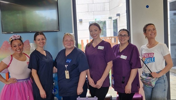 A photo of 4 female members of the team at the proton beam therapy centre at The Christie with a woman dressed as a fairy and a woman holding a magic wand from the charity Spread a Smile.