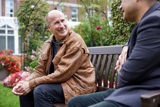 A photo of a male patient sitting on a bench in The Christie garden speaking to a male staff member who is mainly out of shot.