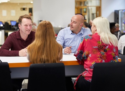 A photo of 2 men talking to 2 women across a table.