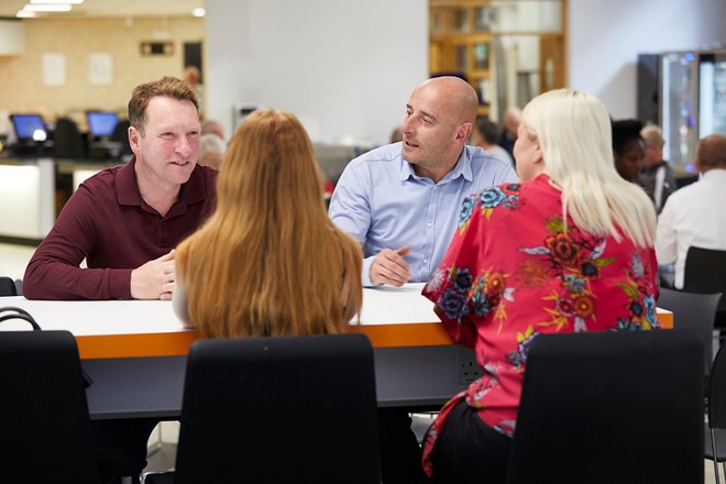 A photo of 2 men talking to 2 women across a table.