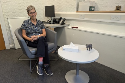 A photo of Anne Crook, recently-retired counsellor at The Christie, sitting next to a coffee table.