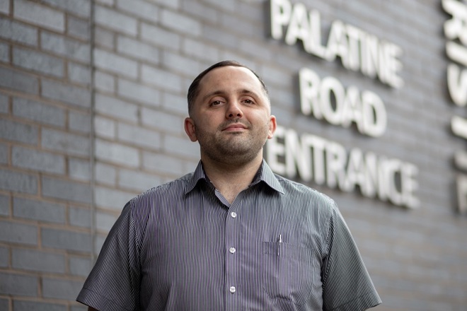 A photo of Sean McGagh, porter at The Christie standing outside the Palatine Road Entrance to the hospital.