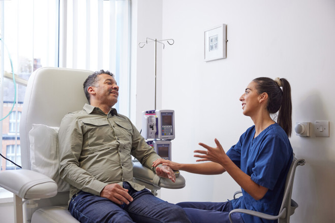 A photo of a female staff member treatment a male patient, who is sitting in a chair.