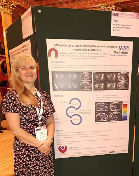 A photo of Christie MR-Linac staff member Lisa McDaid presenting a poster at the annual stereotactic ablative radiotherapy (SABR) consortium meeting. The poster title reads 'MR-guided prostate SABR in patients with unilateral metallic hip prostheses'.