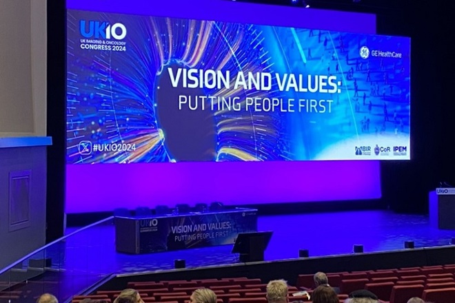 A photo of the presentation screen and stage at the UK Imaging And Oncology Conference 2024, reading 'Vision and Values: Putting People First'.