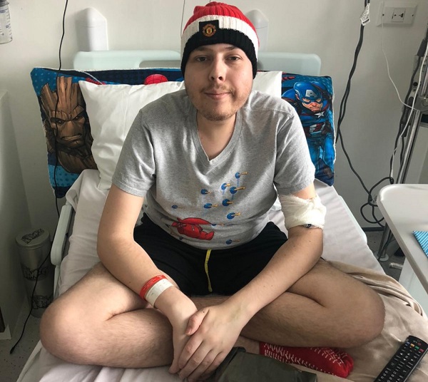 A photo of Christie patient Hamish Graham sitting up in a bed in the teenage and young adult (TYA) unit at The Christie hospital.