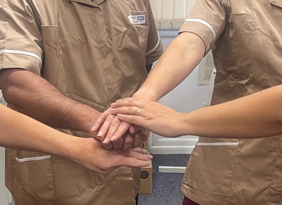 A photo of a group of nursing associates in brown uniforms putting their hands together in the middle of a circle.