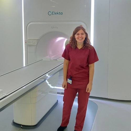 A photo of radiographer Becky standing in front of the MR-Linac machine at The Christie.