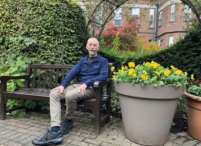 A photo of Christie patient Richard Nelson sitting on a bench in The Christie garden.