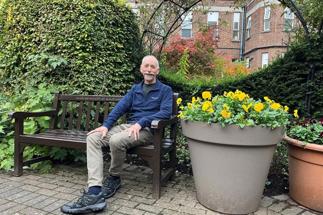 A photo of Christie patient Richard Nelson sitting on a bench in The Christie garden.