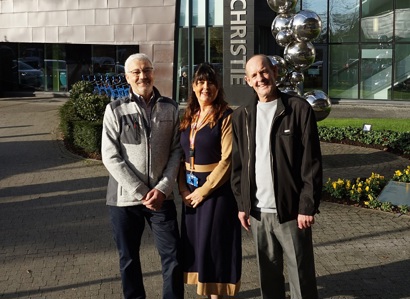 A photo of Christie patients Ian Cameron and Ian Gresty with Christie staff member Charlotte Finchett standing outside The Christie's main entrance.