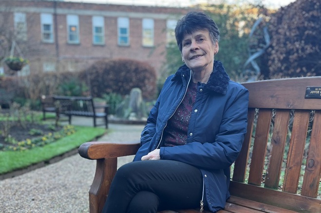 A photo of former Christie patient and supporter Adele Adams sitting on a bench in the garden at The Christie.