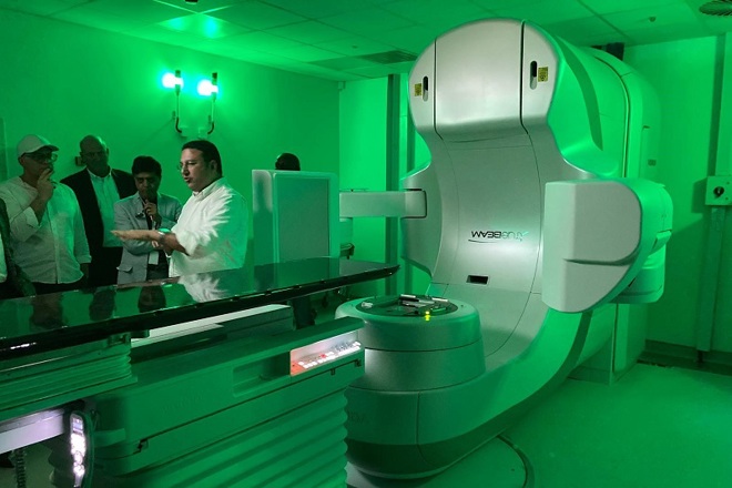 A linear accelerator at the African Medical Centre of Excellence (AMCE) in Nigeria. A group of people are looking at the linear accelerator as a man explains how it works.