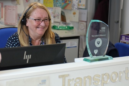 A photo of Linda Thomas, transport co-ordinator at The Christie, wearing a headset and looking at her You Made A Difference award.