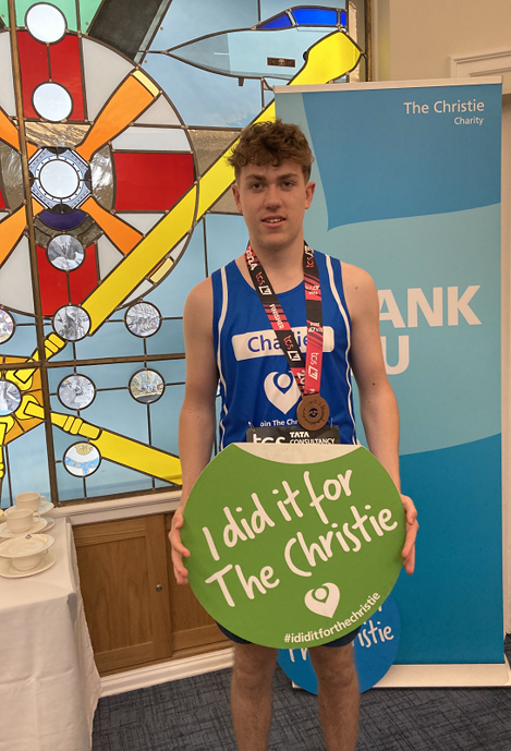 A photo of Christie Charity fundraiser Charlie Balls in a Christie running vest, wearing a London Marathon medal and holding a green 'I did it for The Christie' sign.