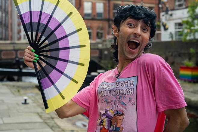 A photo of Christie patient Jay Swinnerton holding a non-binary pride fan and wearing a t-shirt reading 'Trans people wil flourish'.