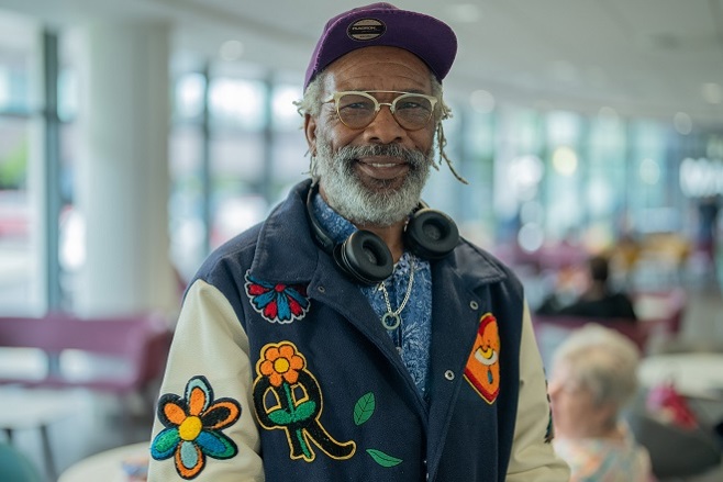 A photo of Christie patient Winston Carrington wearing a colourful bomber jacket and headphones around his neck.