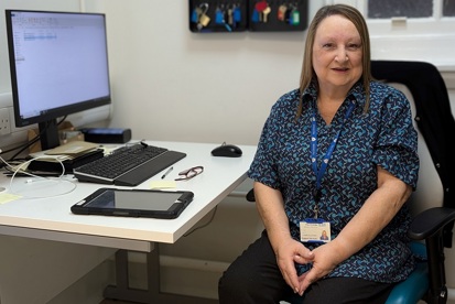 A photo of Angela Keane, domestic supervisor at The Christie, sitting in front of a computer screen.