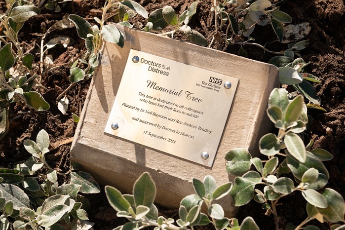 A photo of a Memorial Tree Doctors in Distress plaque at The Christie, reading "This tree is dedicated to all colleagues who have lost their lives to suicide. Planted by Dr Neil Bayman and Rev Andrew Bradley and supported by Doctors in Distress. 17 September 2024".